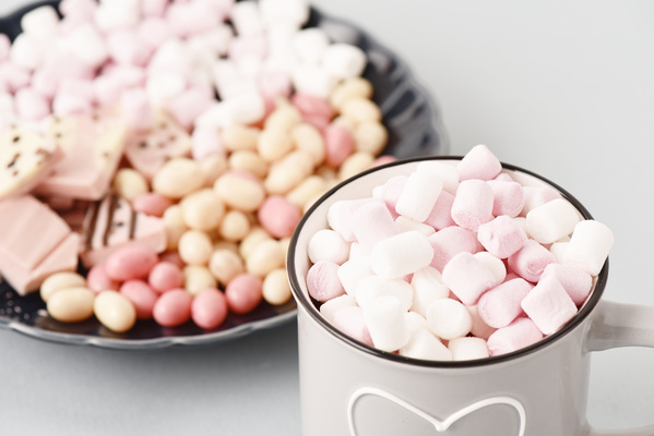 Mug of Marshmallows Stands on Background of Plate of Sweets